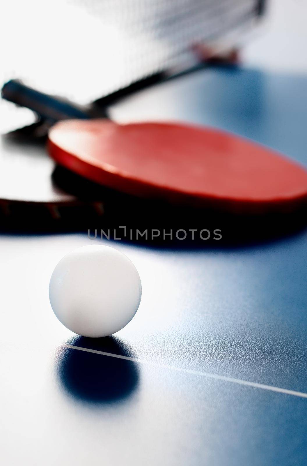 Two tennis rackets and a white ball lie on a tennis table near the net. Active recreation and playing ping pong. Sports background.