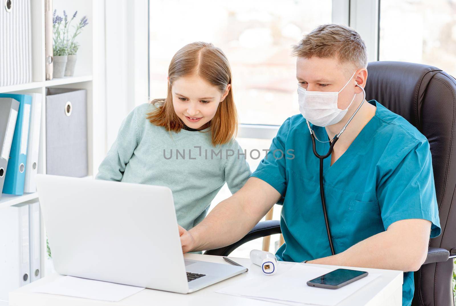 Lovely little girl watching laptop with doctor in clinic