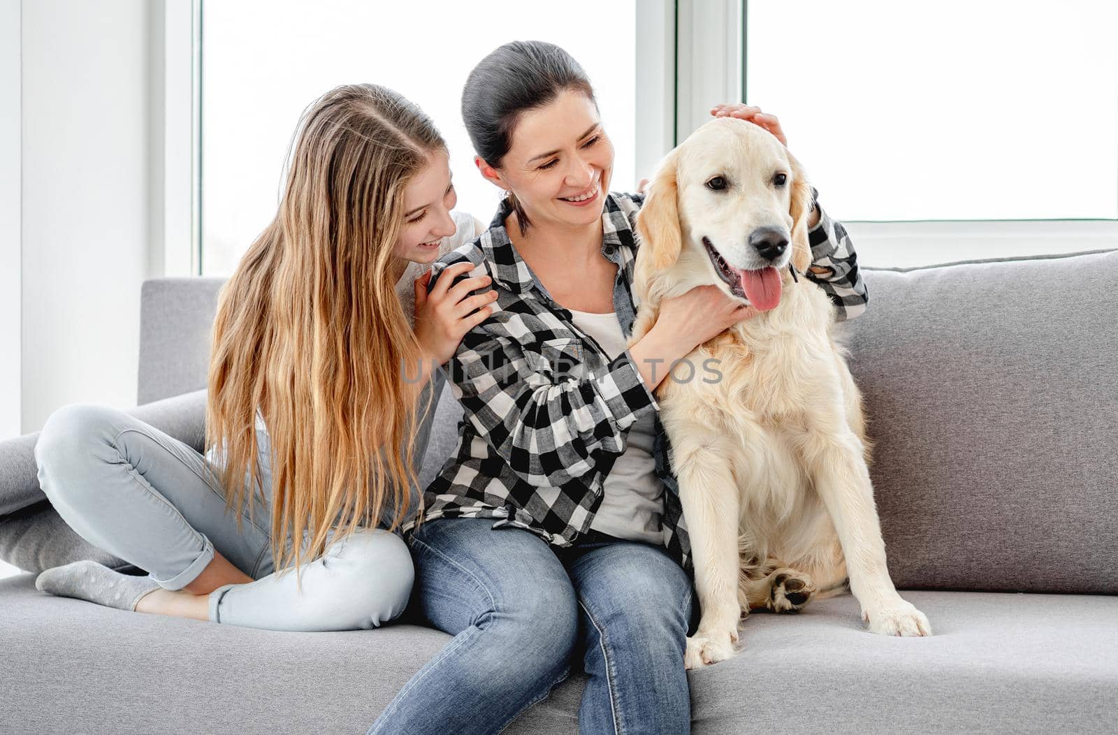 Happy daughter and mother sitting on sofa next to lovely dog