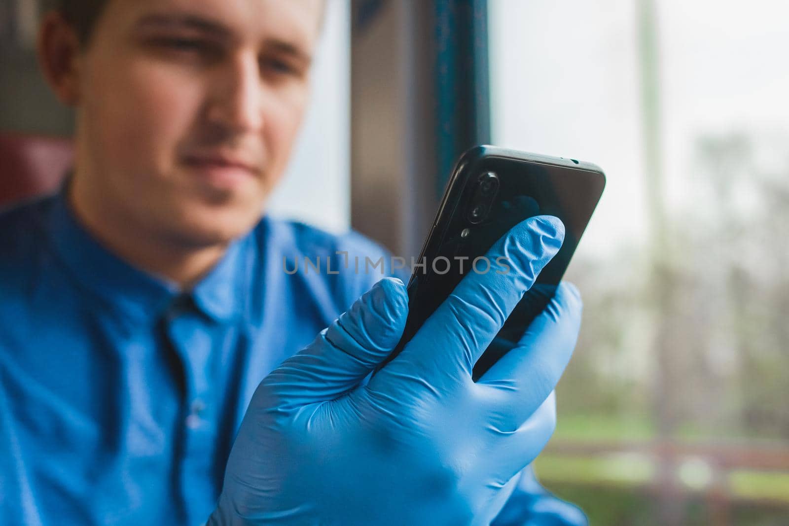 A guy in protective medical glove hold a phone and spends time in it, close-up.