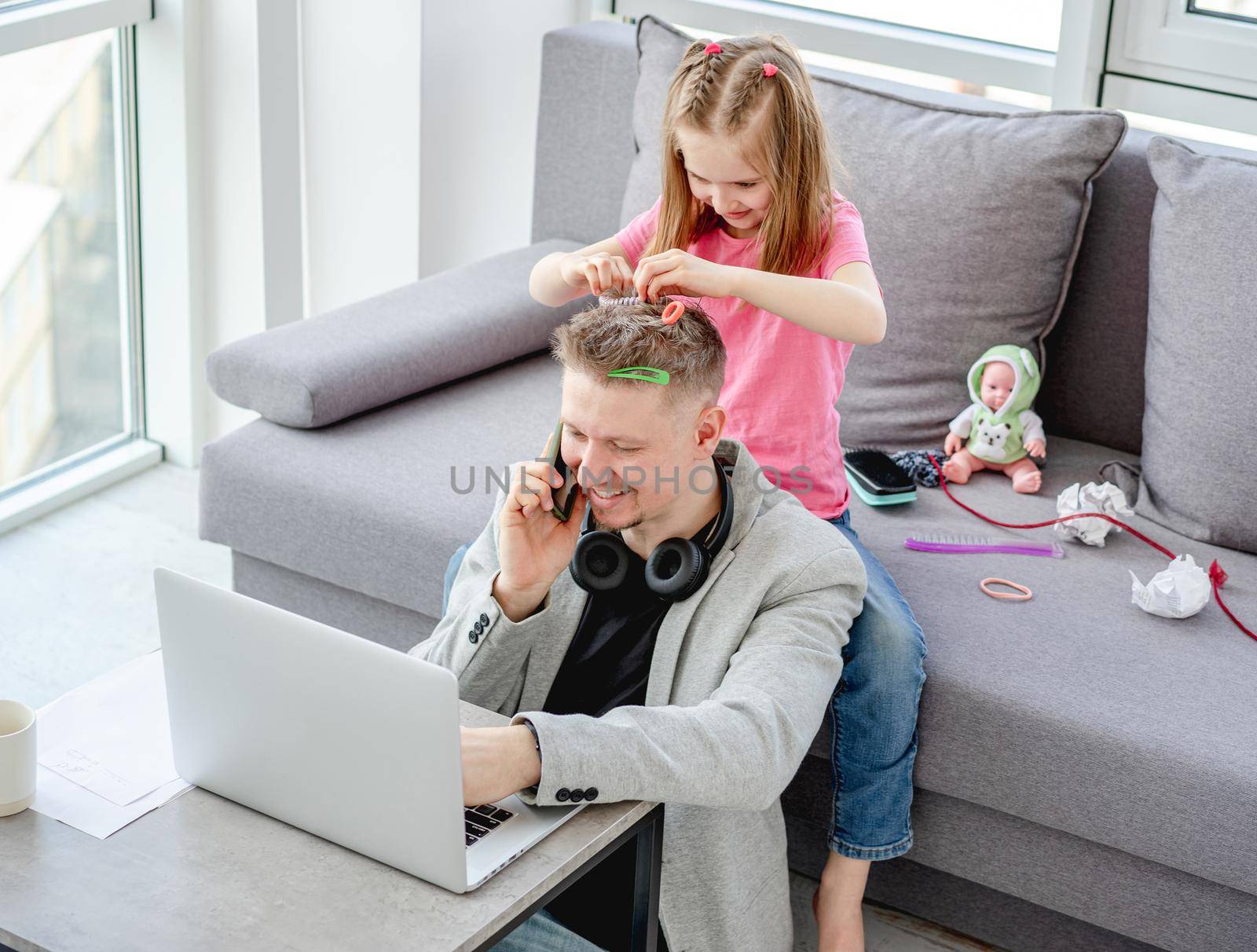 Cute little girl hairstyling man while working at home