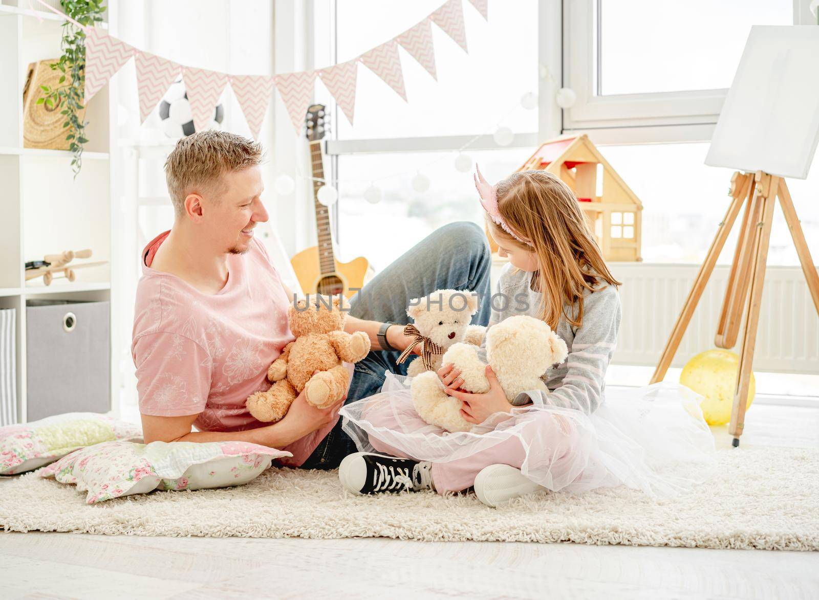 Cute little princess playing with teddy bears with smiling father in children's room