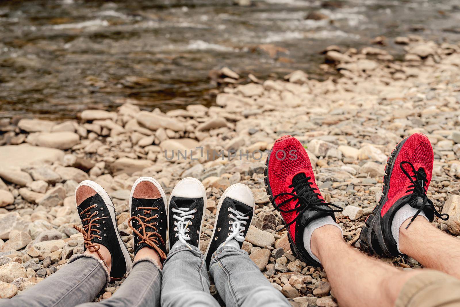 Tree pairs of legs in black gumshoes resting on stones outdoors