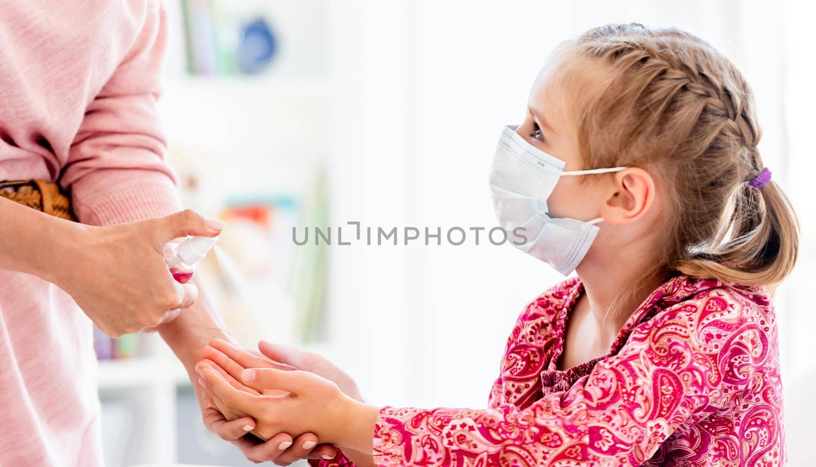 Teacher spraying sanitizer on little girl's hands at school during quarantine