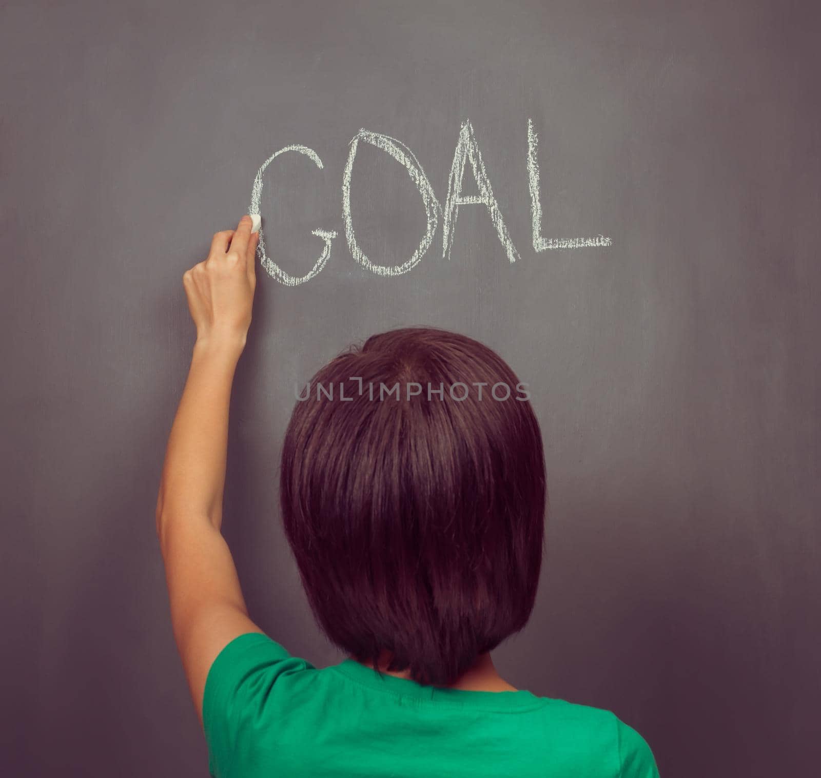Unrecognizable woman writes the word goal on the blackboard, rear view