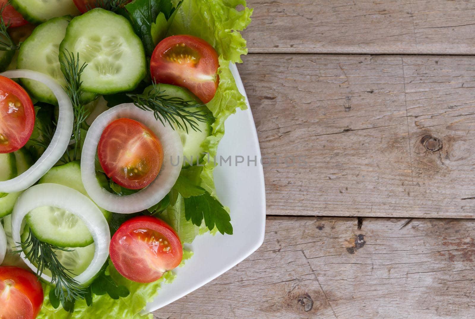 Fresh salad from vegetables, herbs, on a wooden table, top view. Space for text