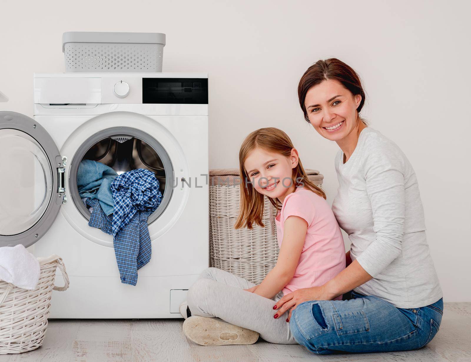 Happy mother and little daughter washing clothes using machine in light room