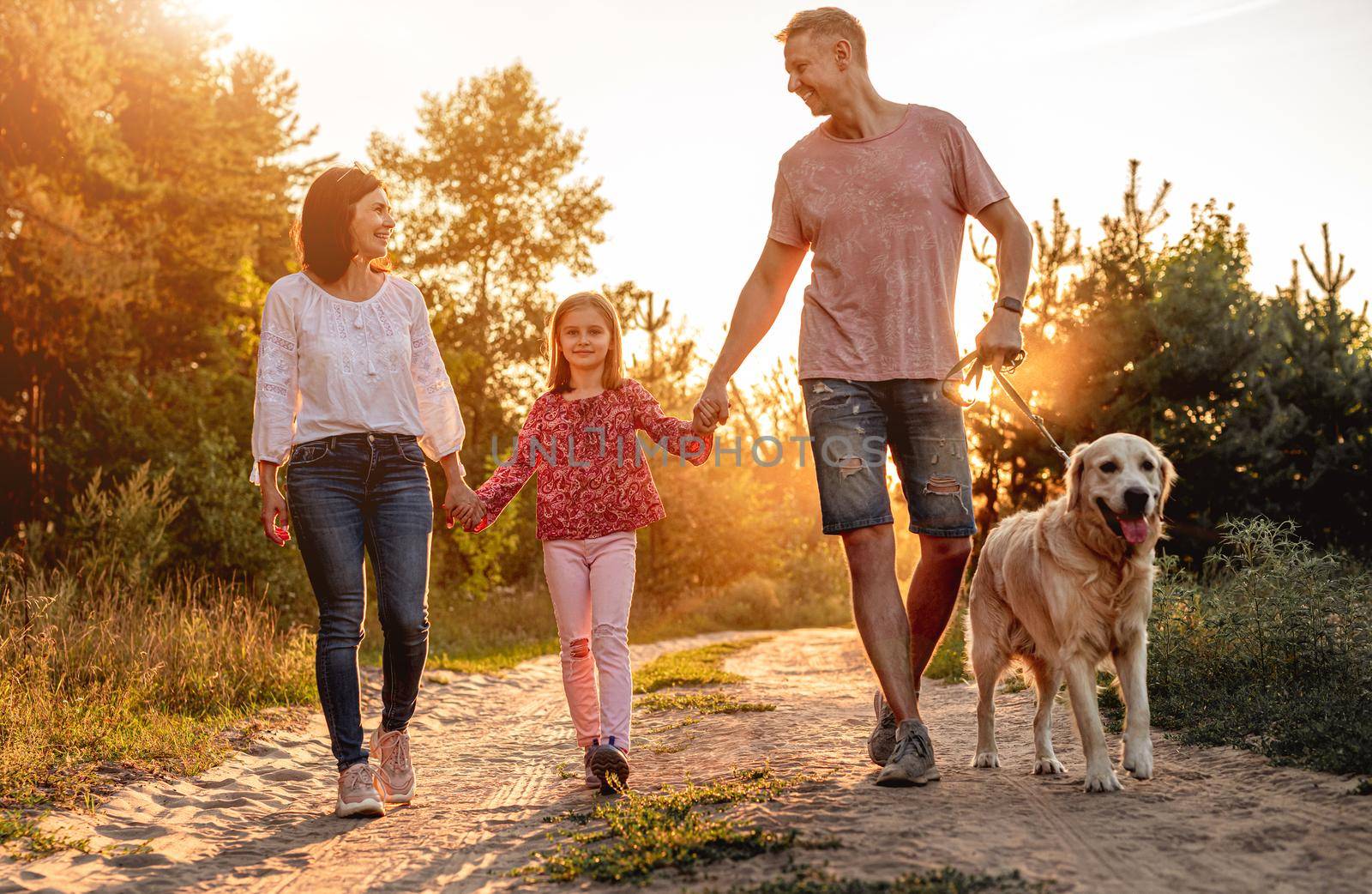 Family with dog walking along ground road outdoors at sunset