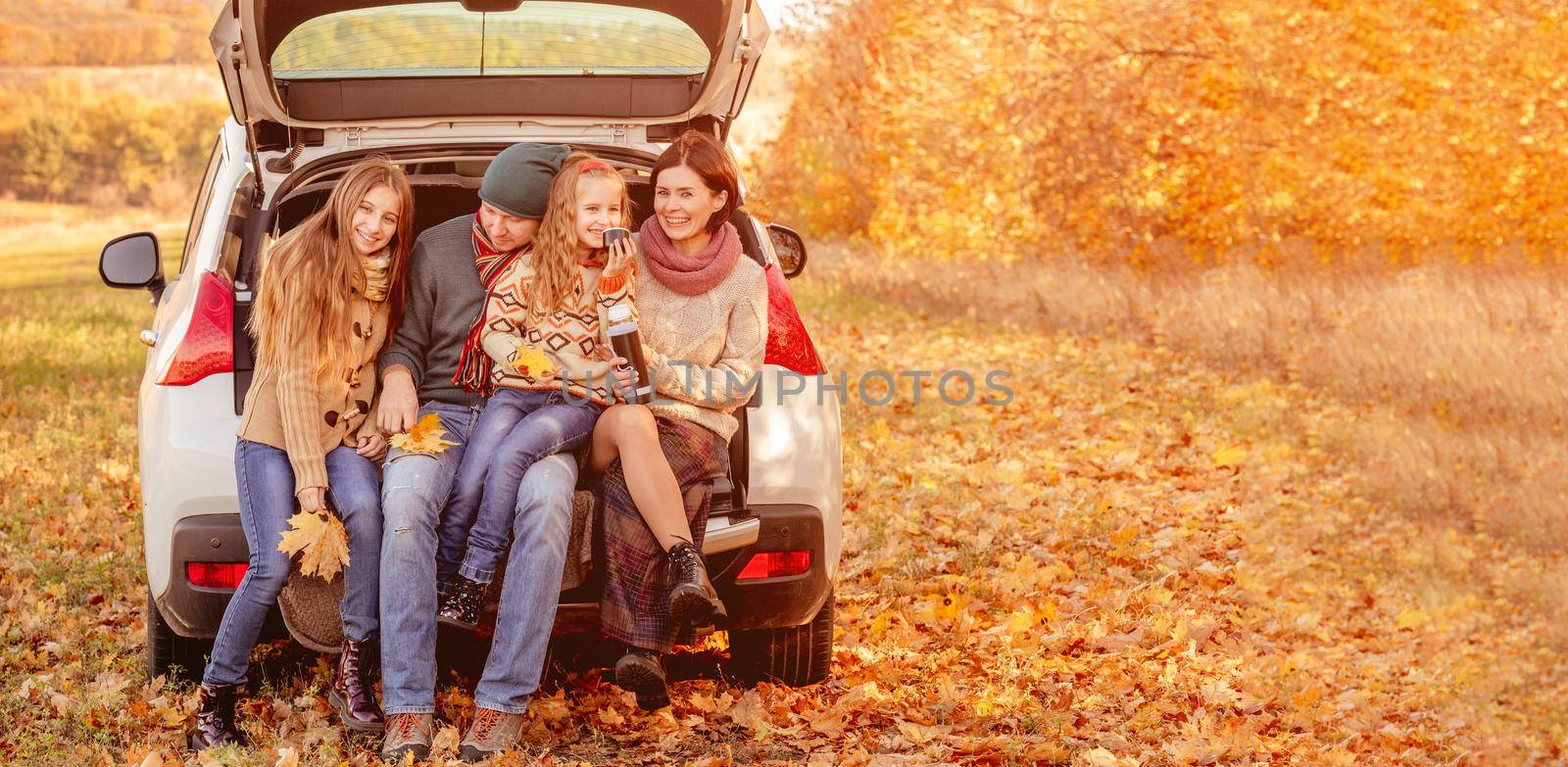 Beautiful family resting in car trunk on autumn background