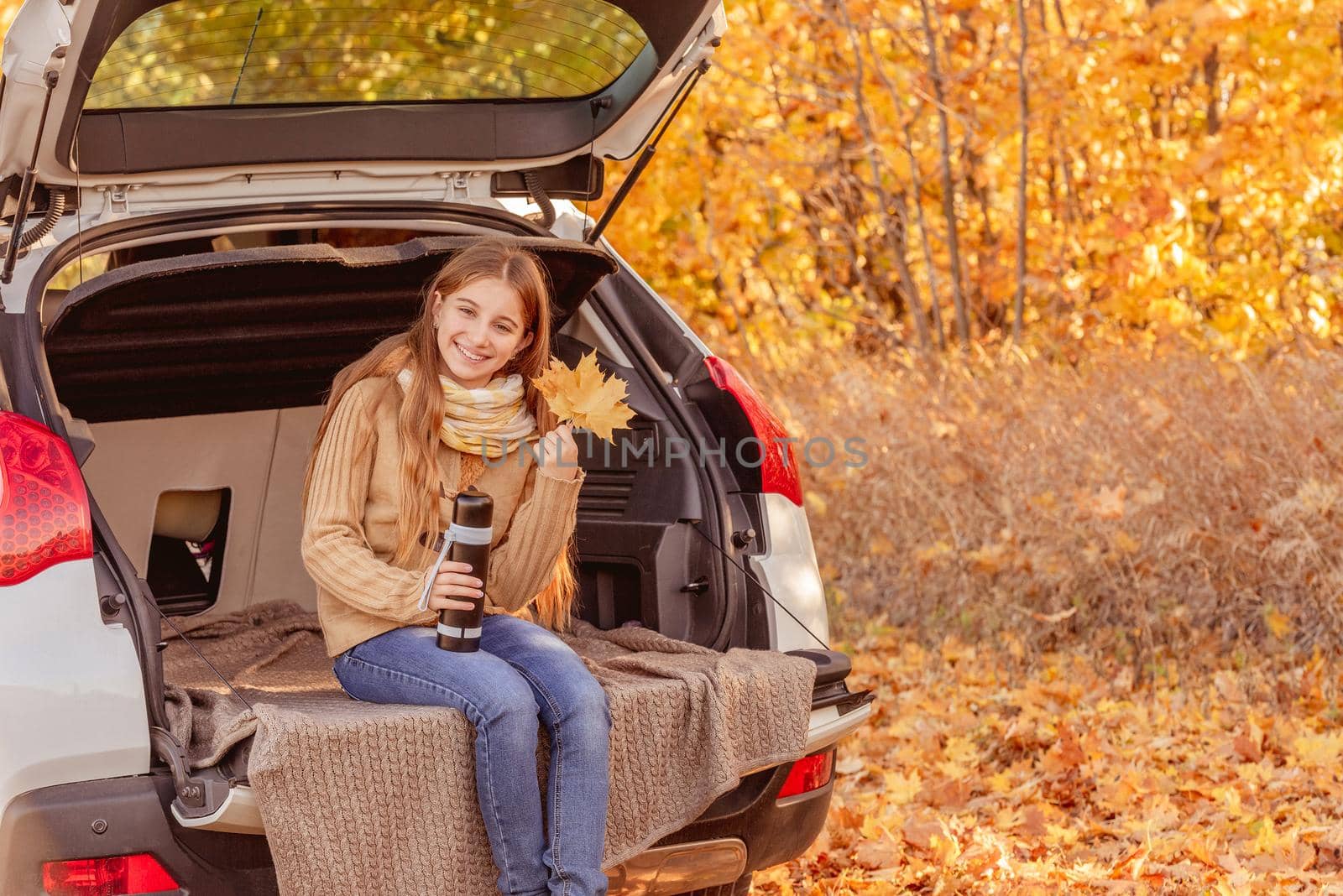 Pretty girl sitting in car trunk in autumn park