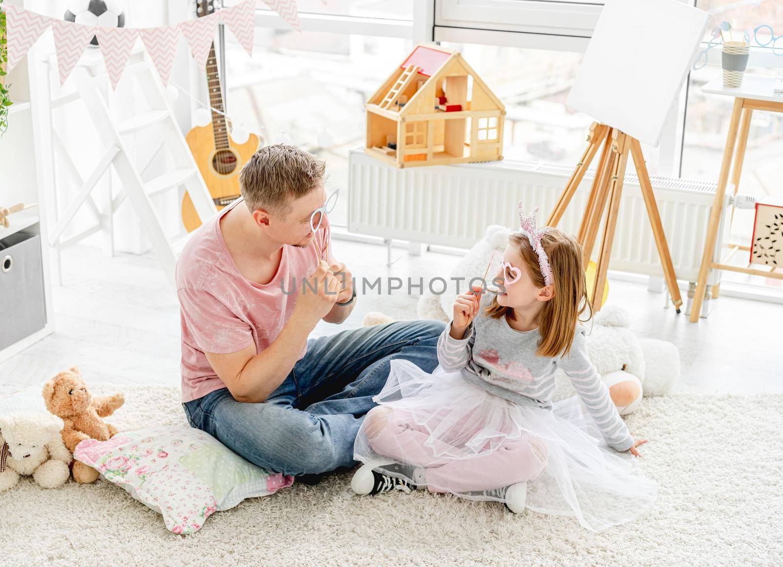 Smiling man and happy girl fooling with glasses on stick indoors