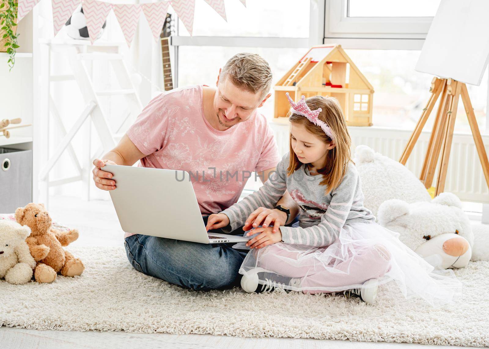 Handsome father teaching pretty daughter to work on laptop in children room