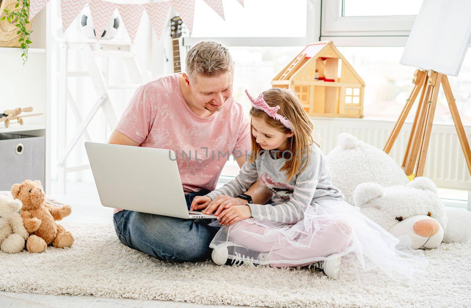 Handsome father teaching beautiful little daughter to use laptop at home