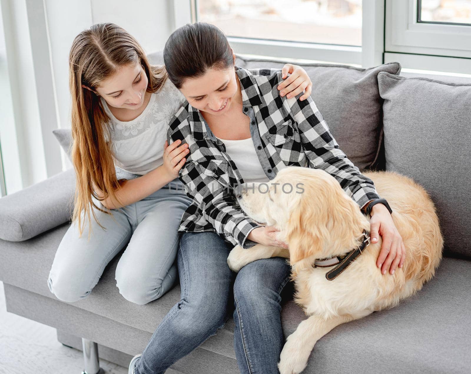 Happy daughter and mother sitting on sofa next to lovely dog