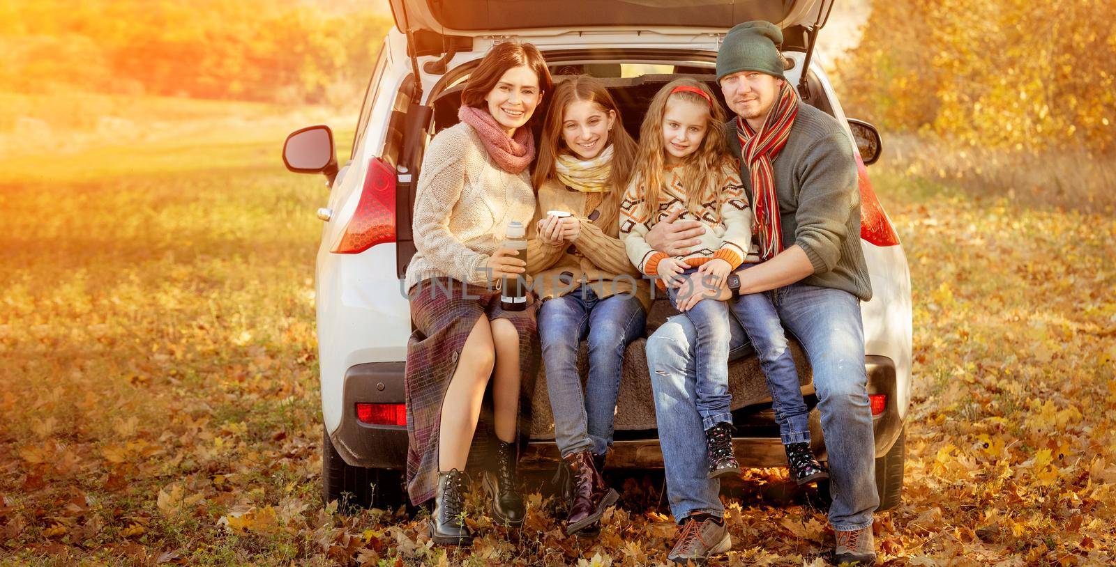 Happy family sitting in car trunk on autumn background