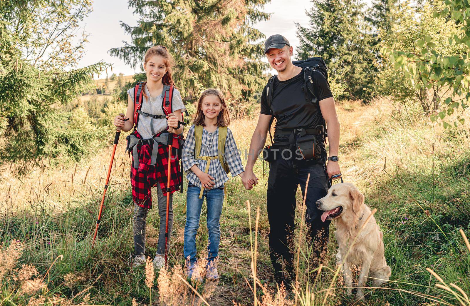 Smiling father with daughters and dog hiking sunny mountain