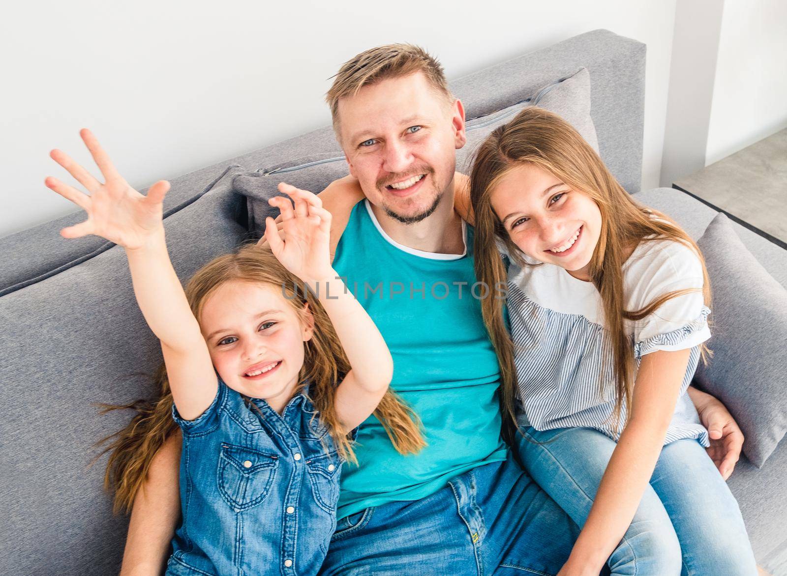 Lovely family of dad and two sisters are spending free time on the couch in the living room