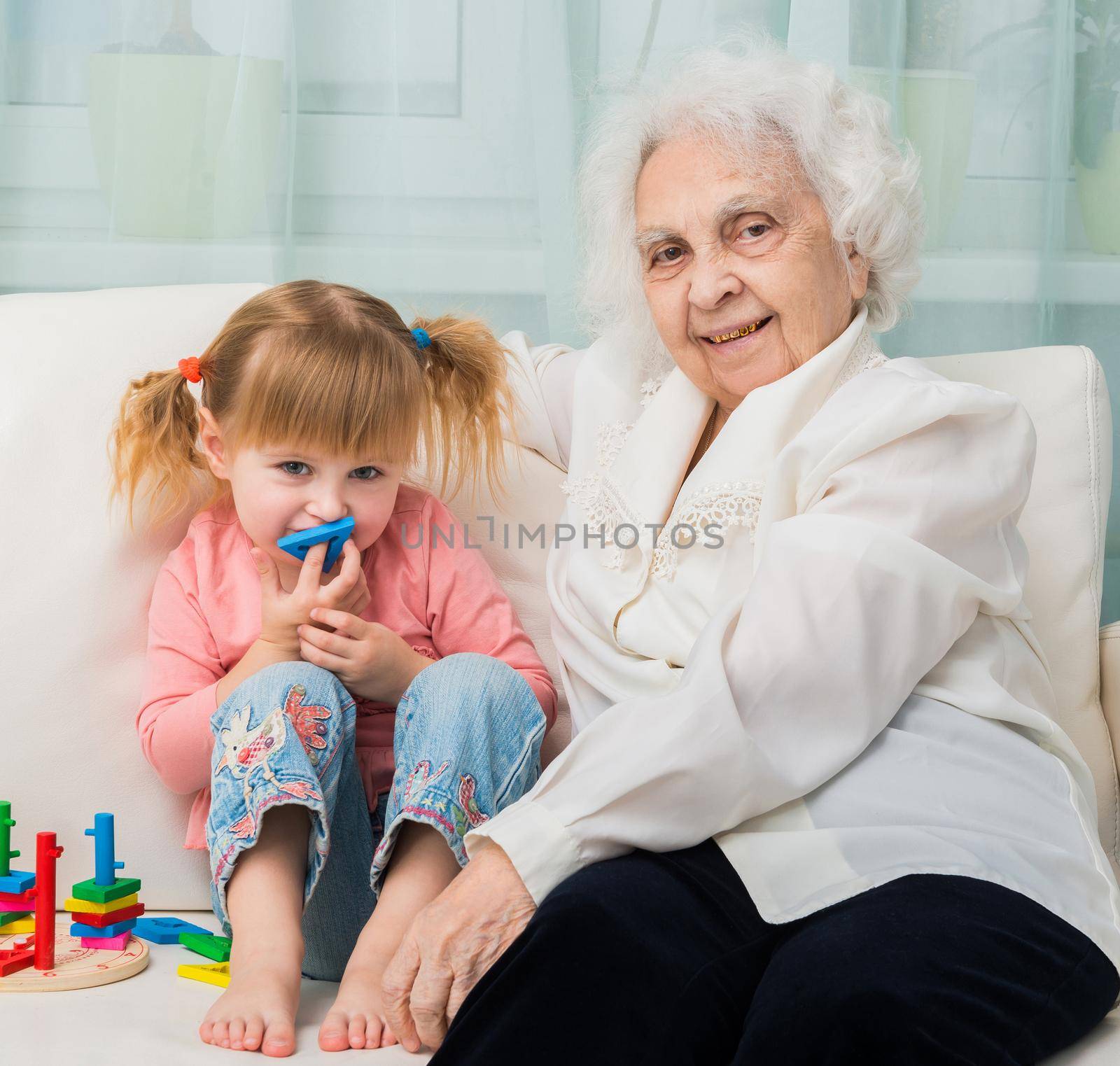 little girl with grandmother sitting on a sofa with toys