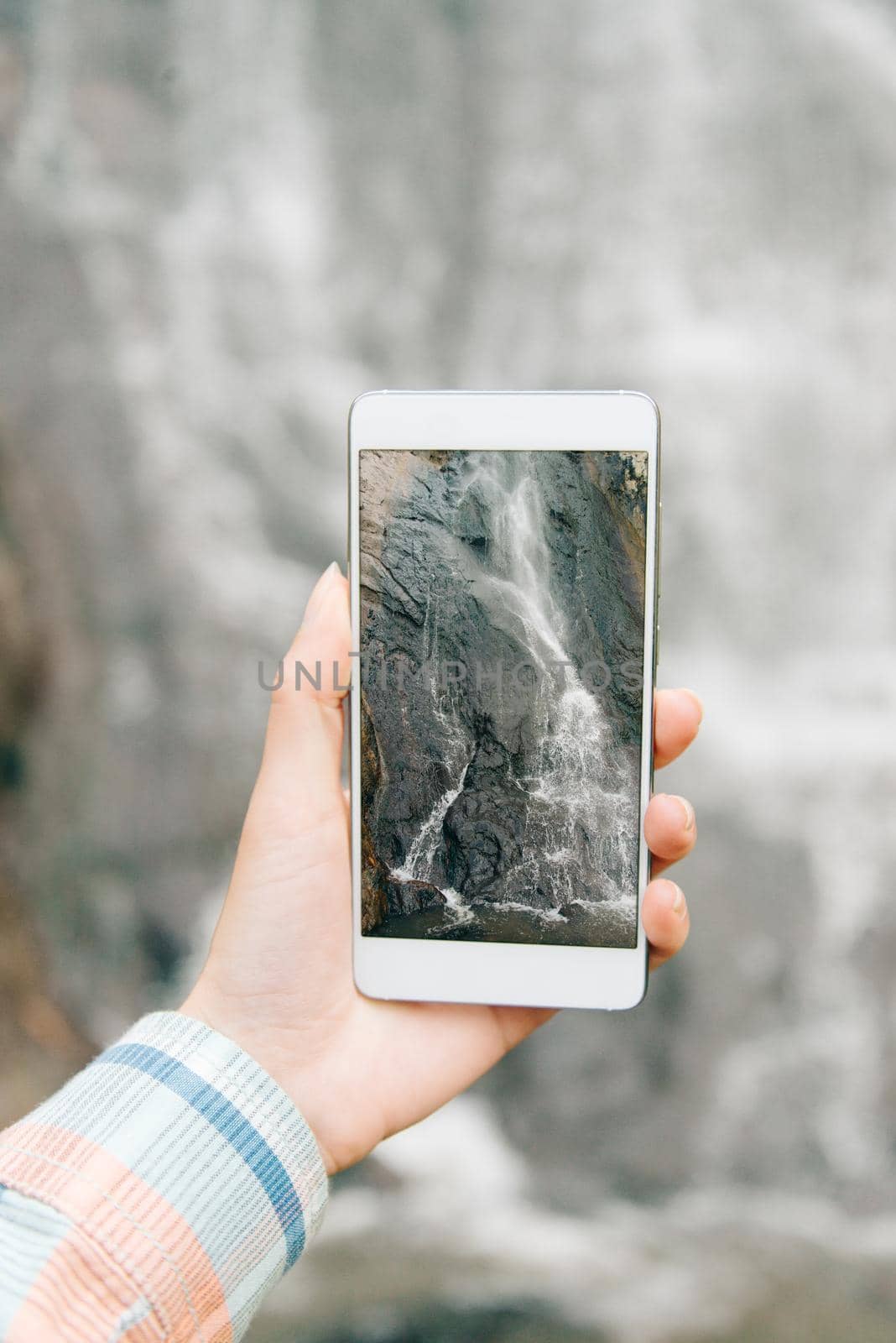 Woman taking photo with smartphone the waterfall outdoor, view of hand, pov image.