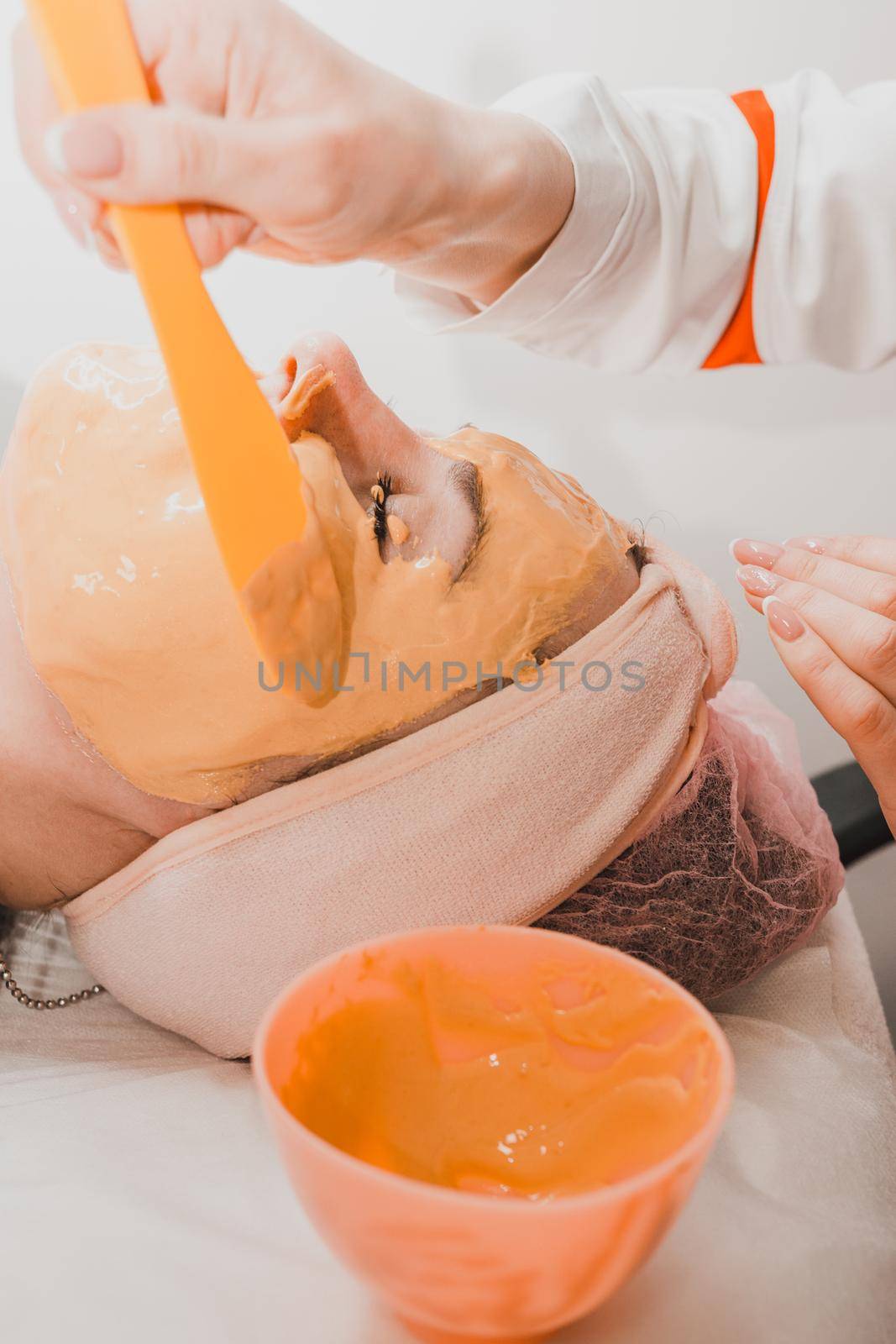 Using a gold mask in cosmetology, a woman at a beautician applying a gold mask on her face. by Niko_Cingaryuk