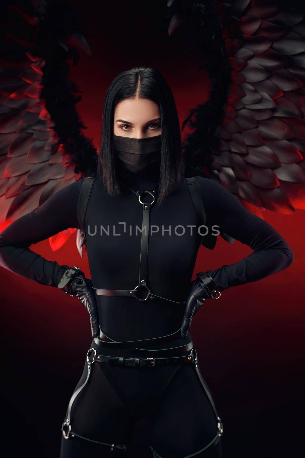 the woman in a black bodysuit with leather straps and black wings on a dark red background
