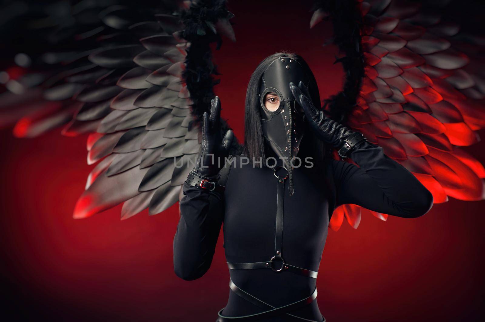 a woman wearing a plague doctor mask with leather straps and black wings on a dark red background by Rotozey