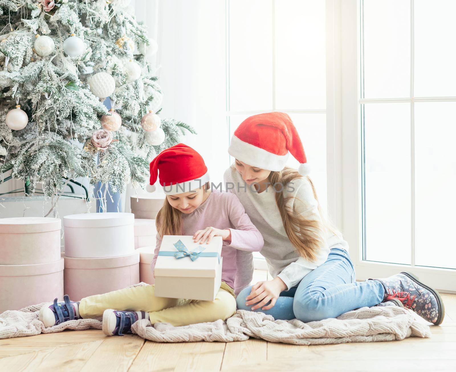 Smiling sisters in santa hats opening new year gifts