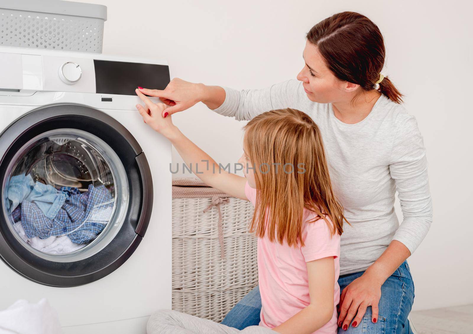 Mother teaching daughter how to operate washing machine in light bathroom