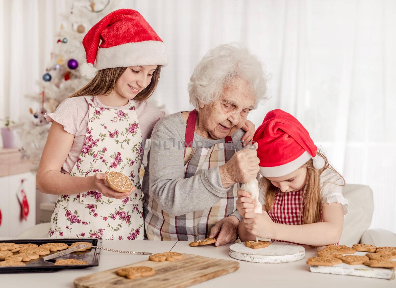 Grandmother with granddaughters in santa hats decorating cookies with cream