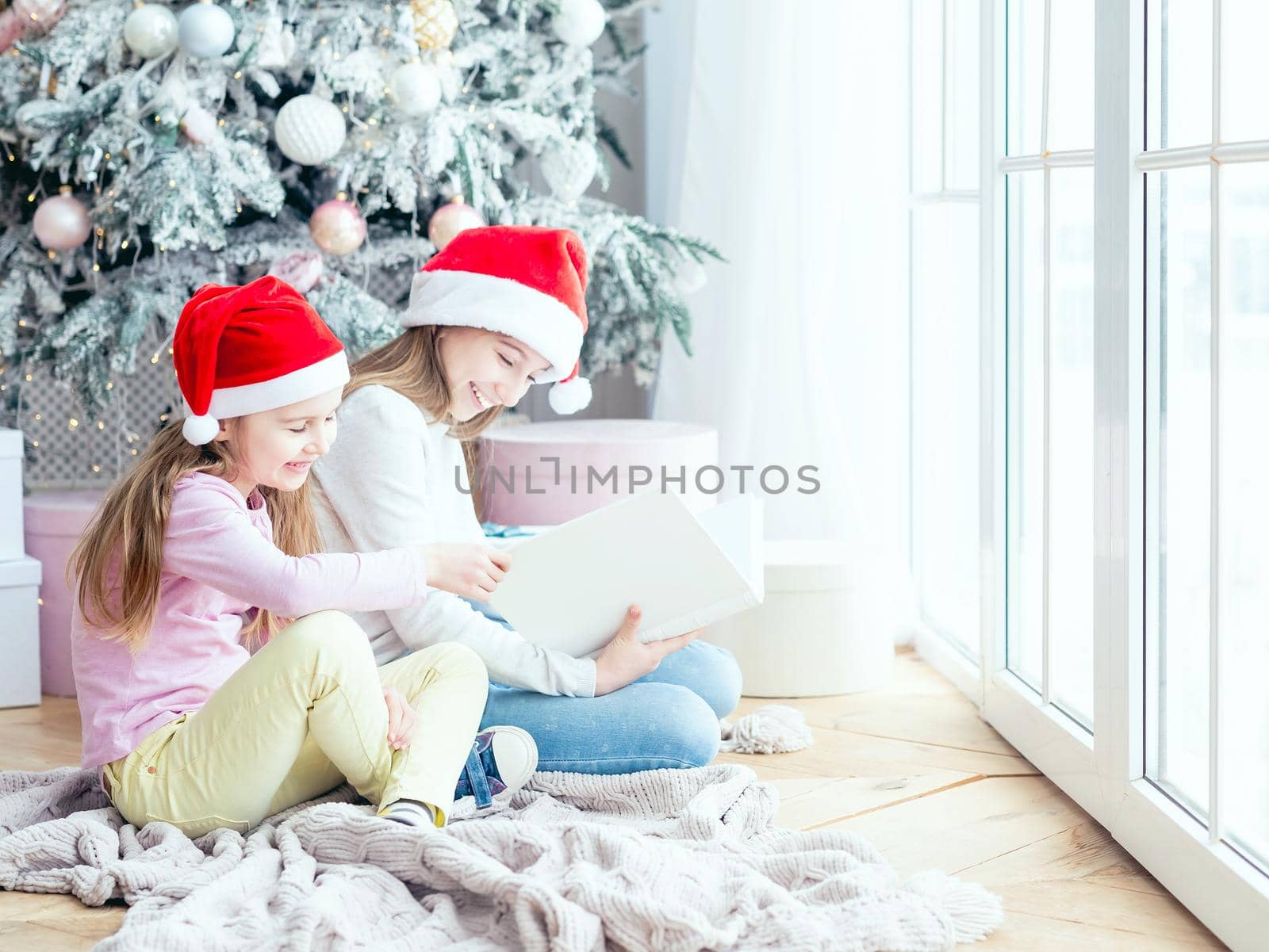 Smiling sisters in santa hats reading book of desires