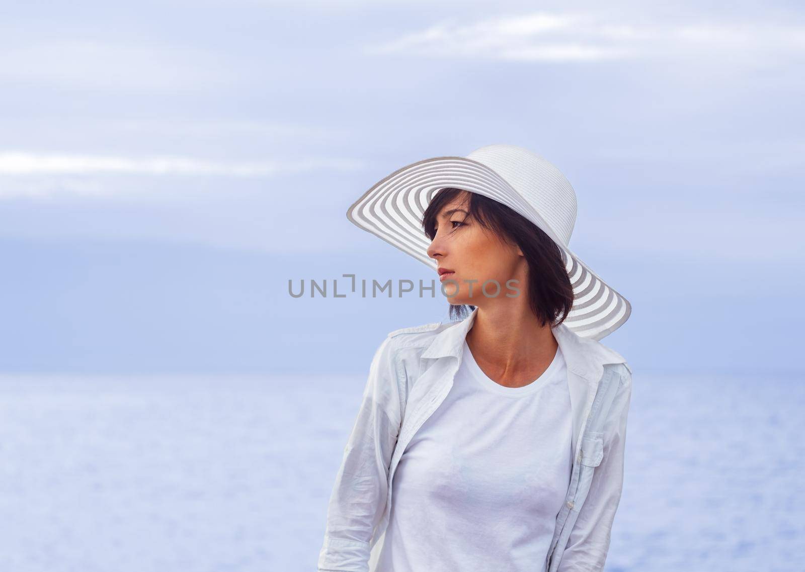 Young woman in a hat with a wide brim stands on the the beach