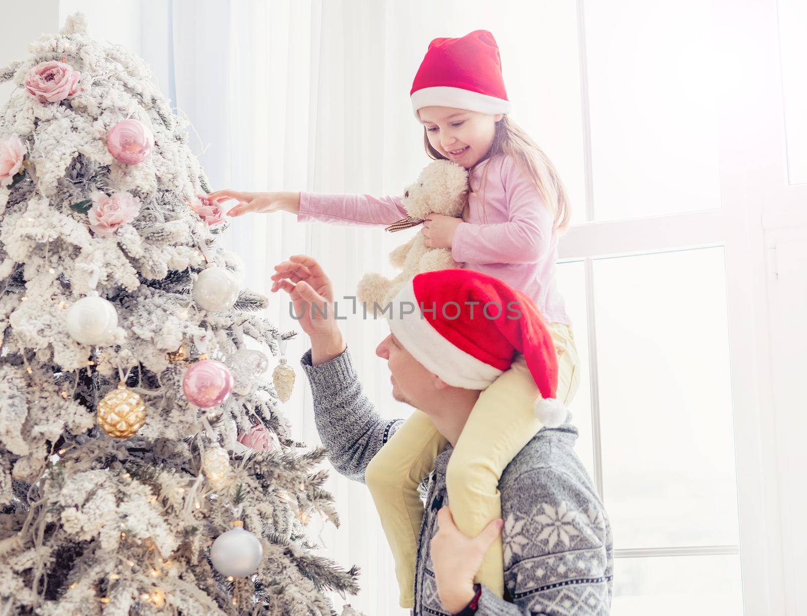 Father holding daughter near christmas tree by tan4ikk1