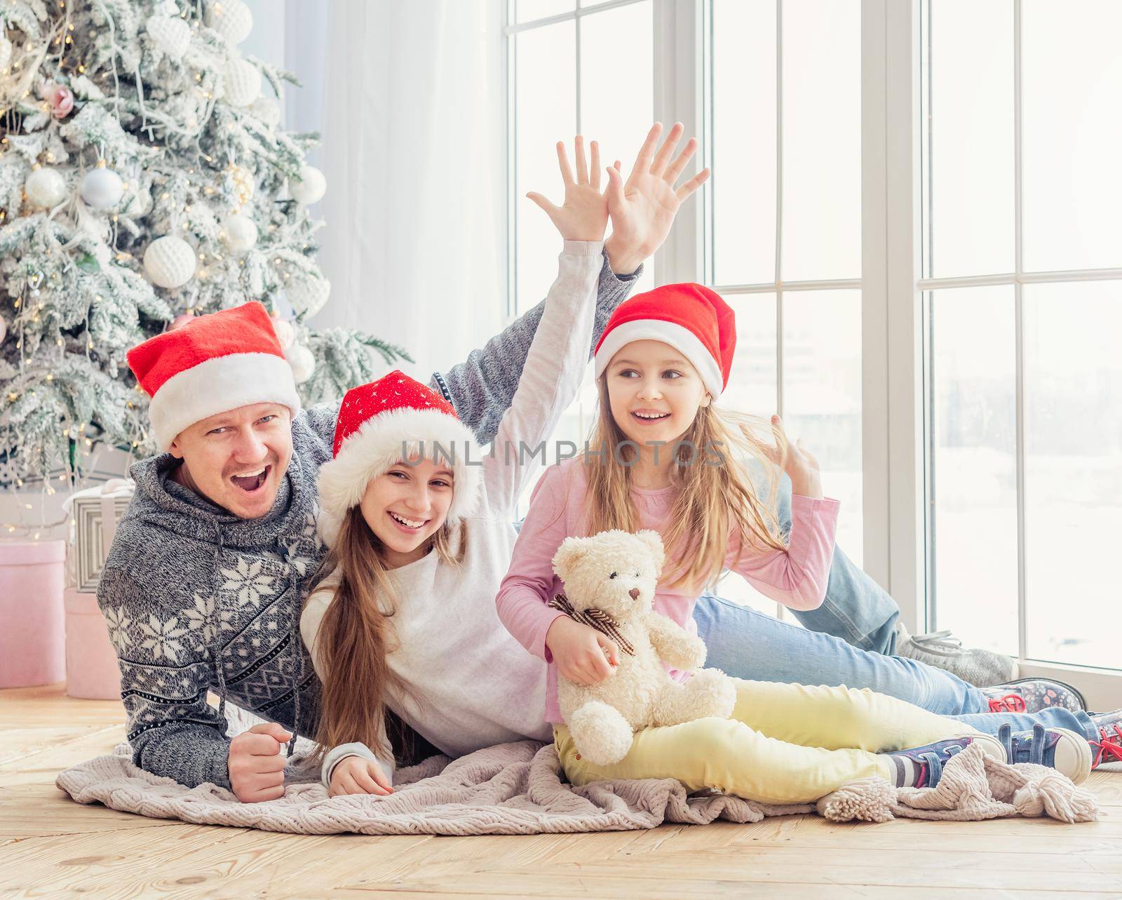 Smiling family in santa hats lying together near christmas tree
