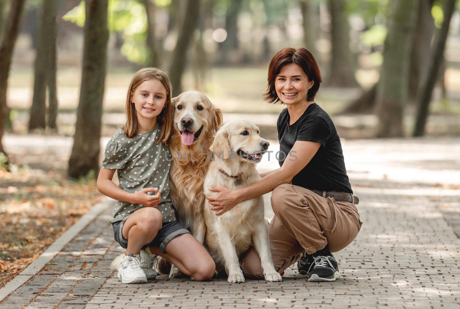Mother and daughter with golden retriever dogs in the park. Family with pets doggies and preteen girl child outdoors