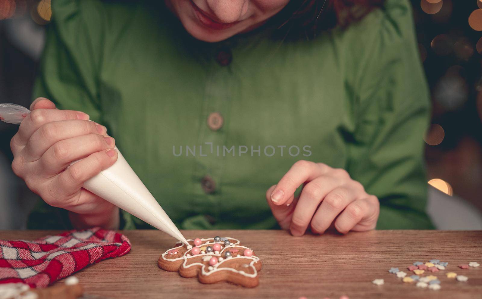 Girl in festive apron decorating gingerbread snowflake using culinary bag at home