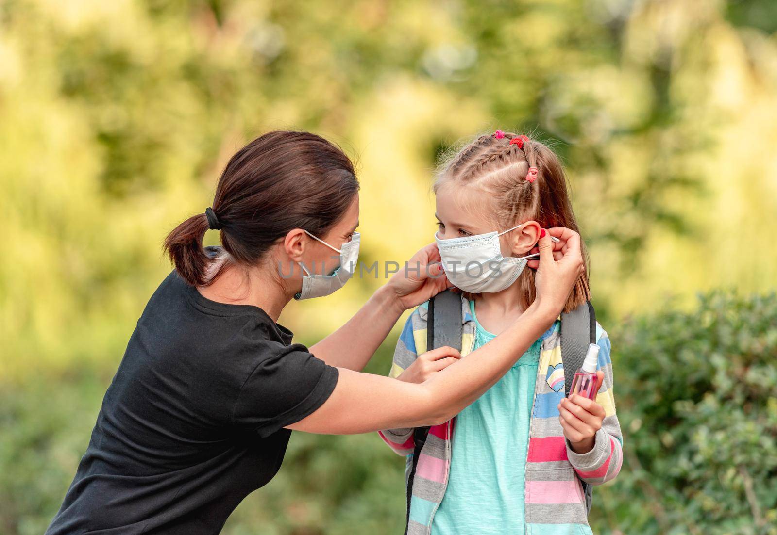 Mother putting protective mask on little daughter before going back to school