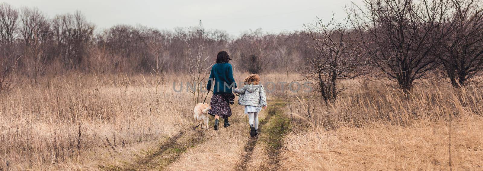 Mother and daughter walking dog along dirt road