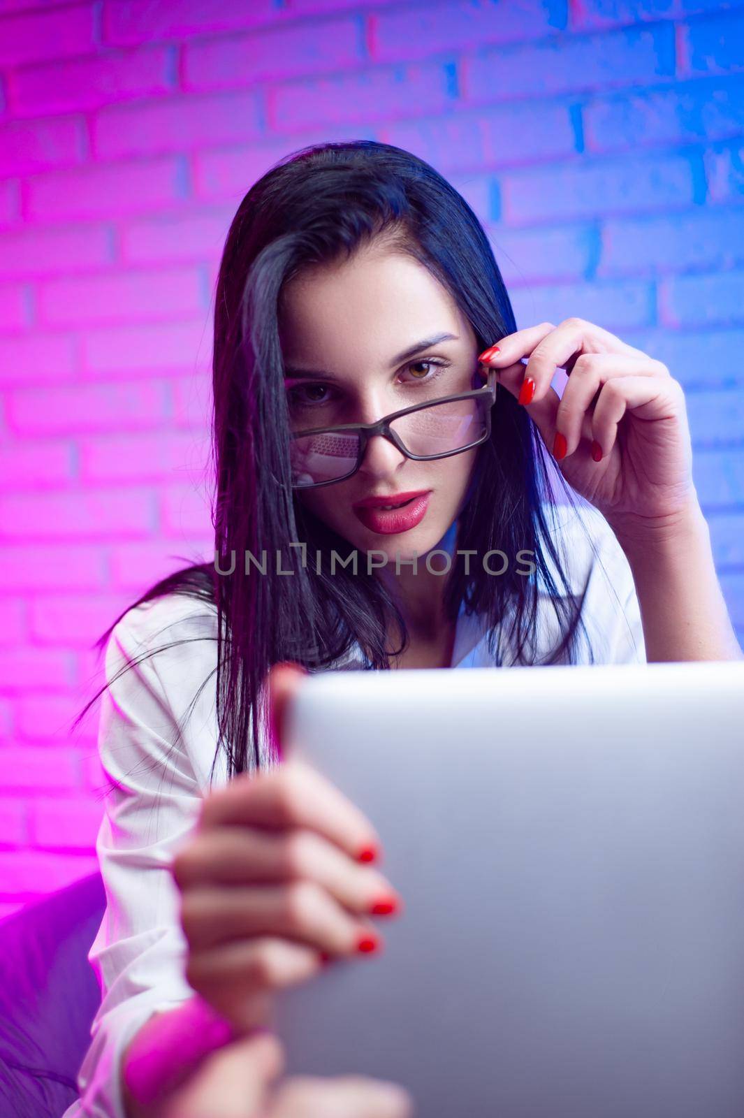 woman with glasses in a white shirt in a neon light with a laptop