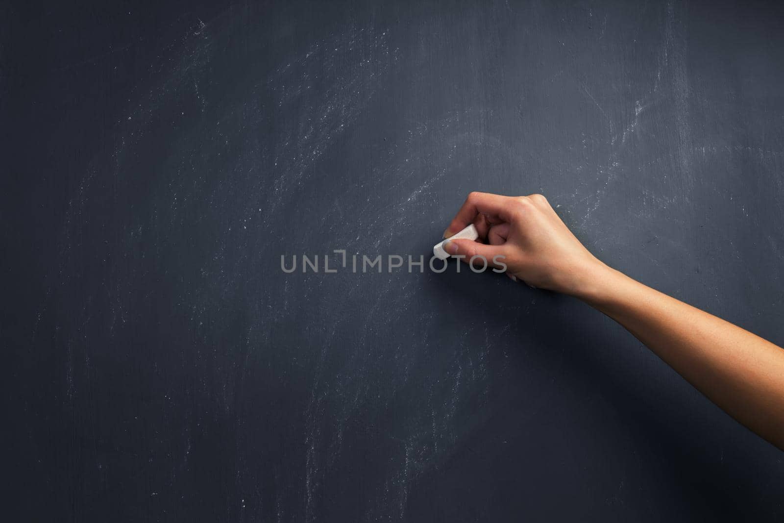 The human hand starts writing with chalk on a clean blackboard