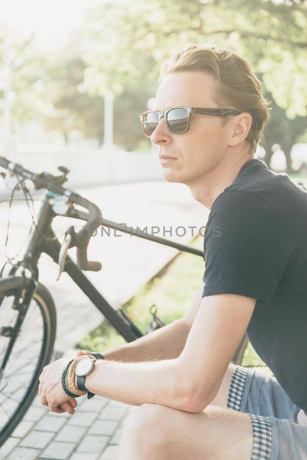 Handsome cyclist young man in sunglasses rests in summer park.