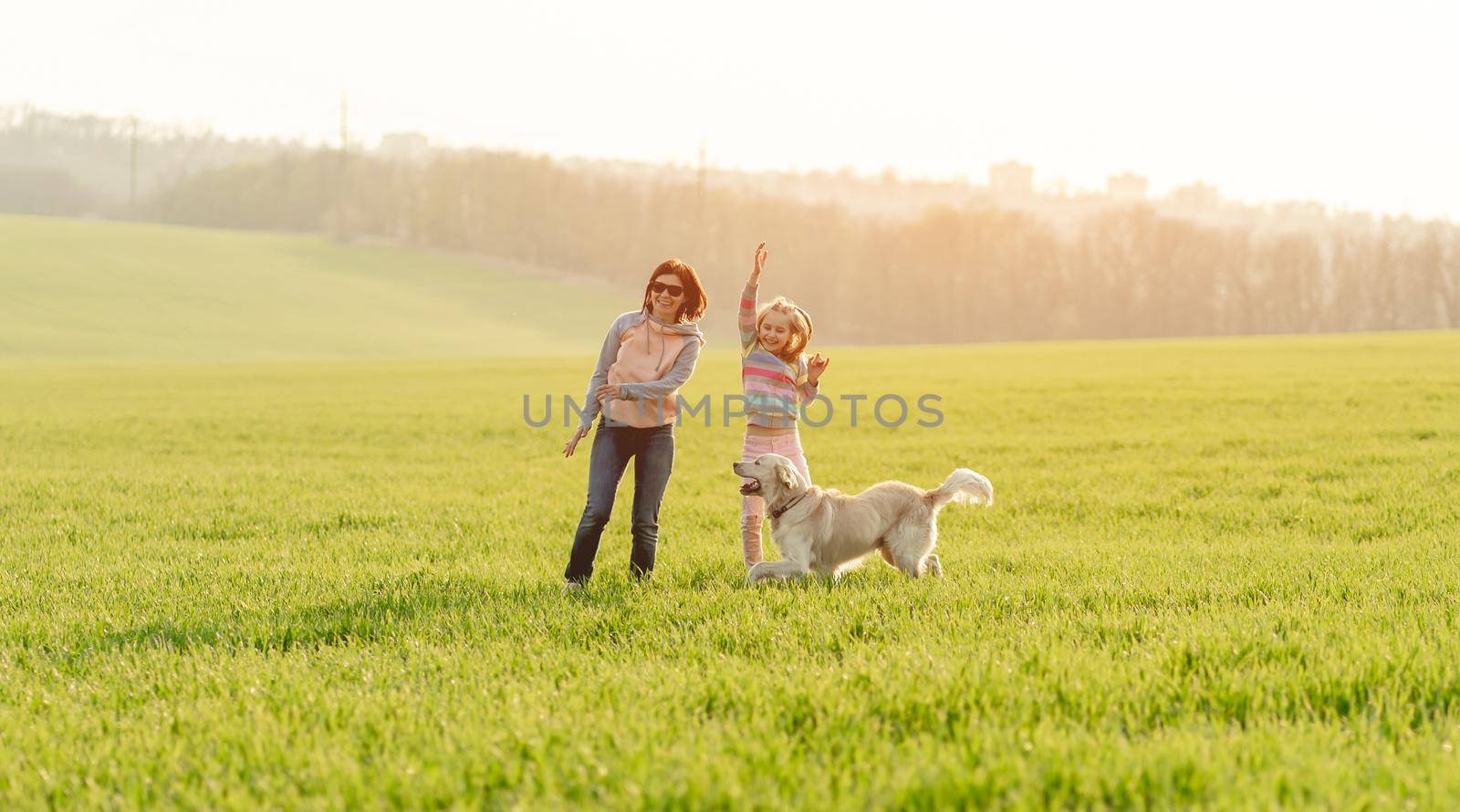 Happy woman and cute girl playing with lovely dog outdoors