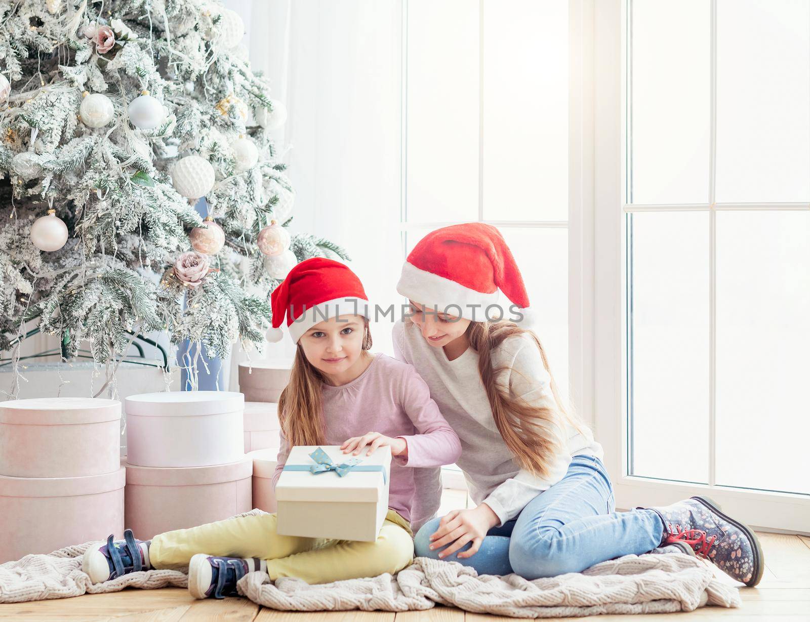 Smiling sisters in santa hats opening new year gifts