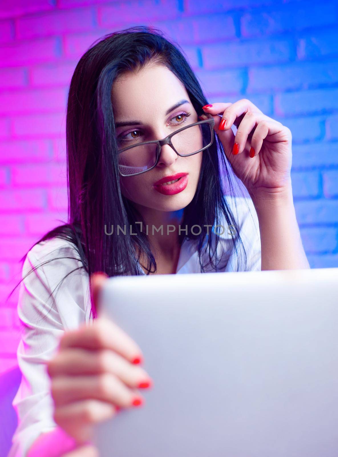 a woman with glasses in a white shirt in a neon light with a laptop by Rotozey