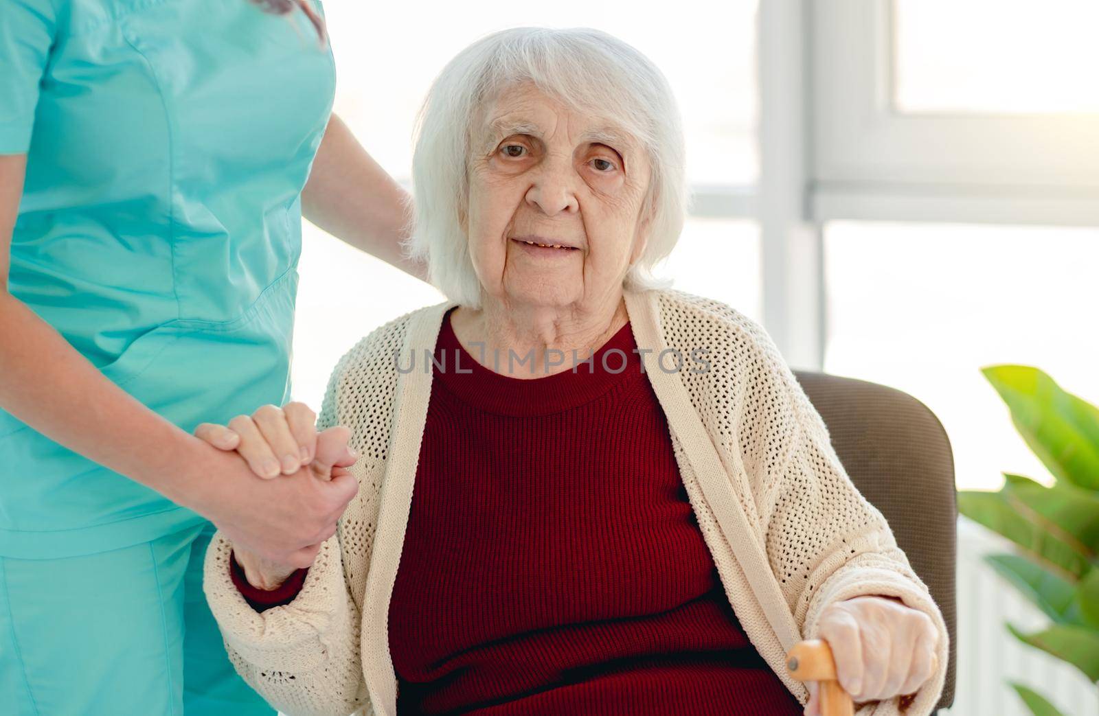 Old lady leaning on nurse hand to stand from chair in nursing home