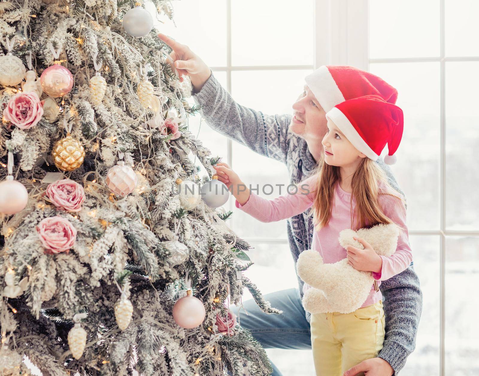 Father with little daughter in santa hats looking at christmas tree decorations