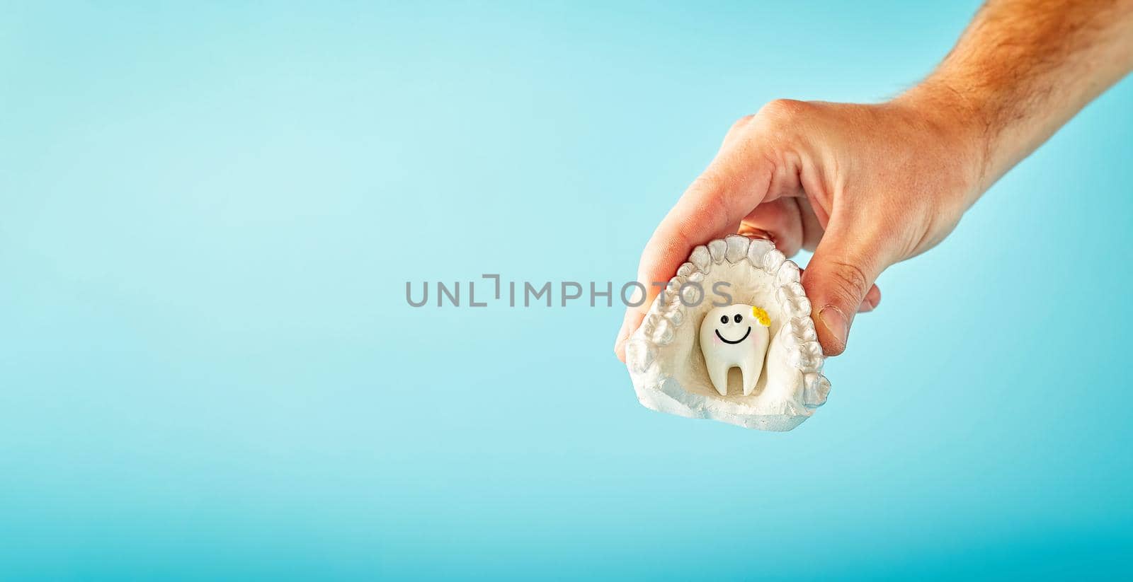 A man is holding a tooth on a blue background. Visit to the dentist, stomatology advertising concept, dental health