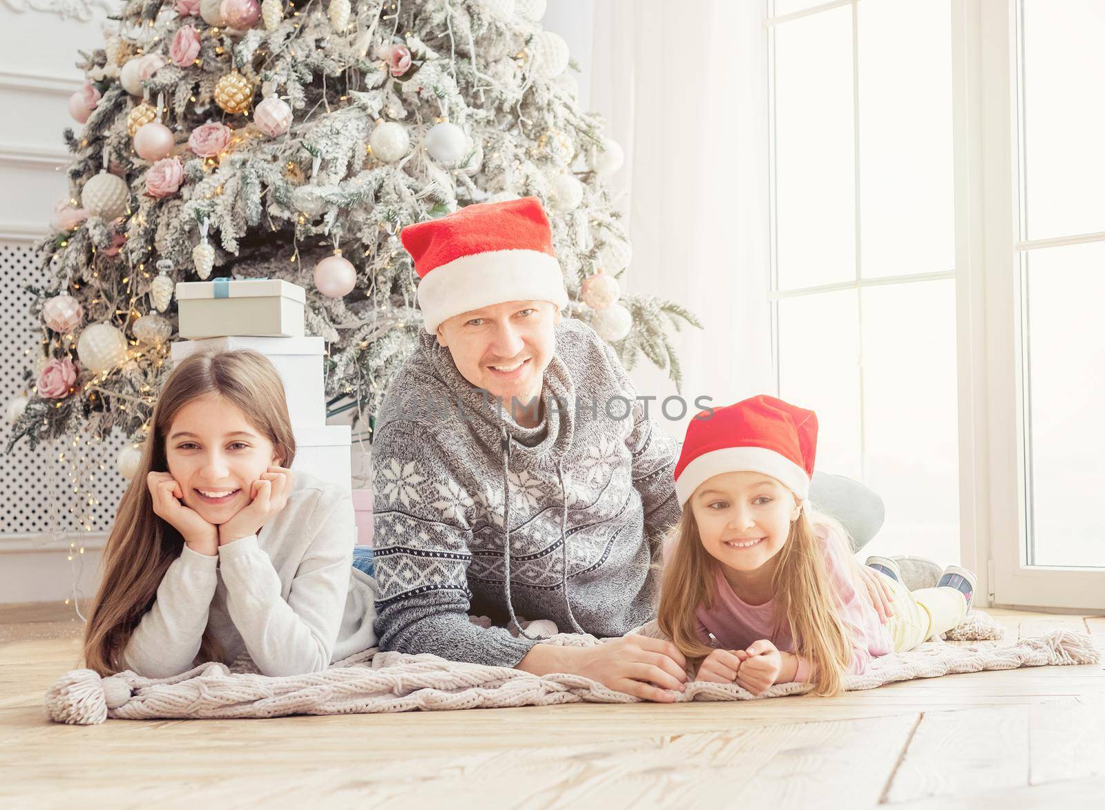 Smiling father with daughters lying together near christmas tree