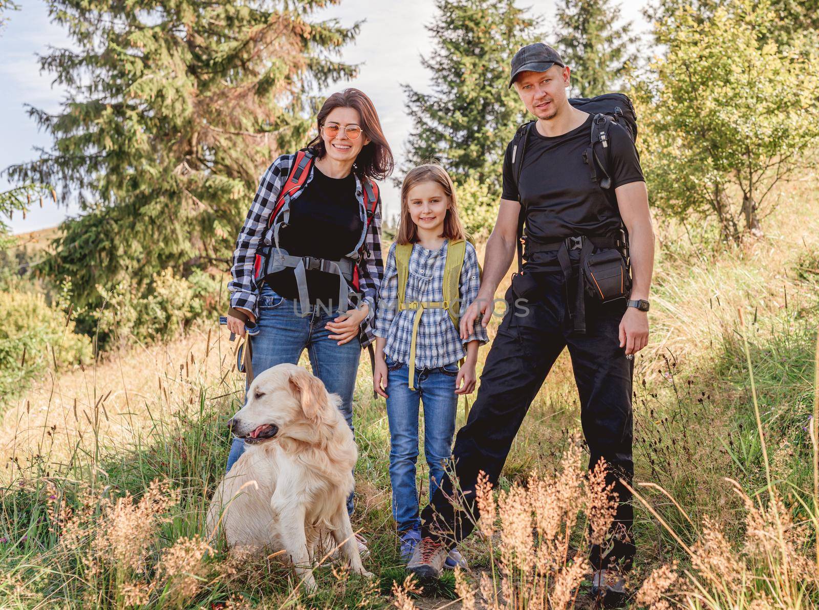 Happy family trekking in sunny mountains with dog in summer