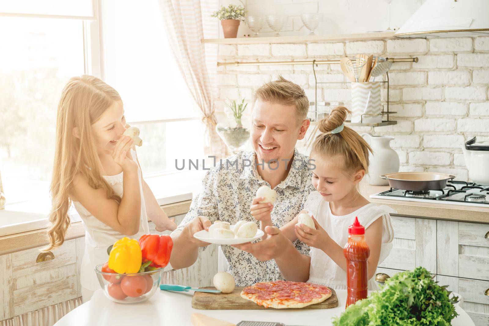 Dad with two small daughters preparing pizza with mushrooms in the kitchen