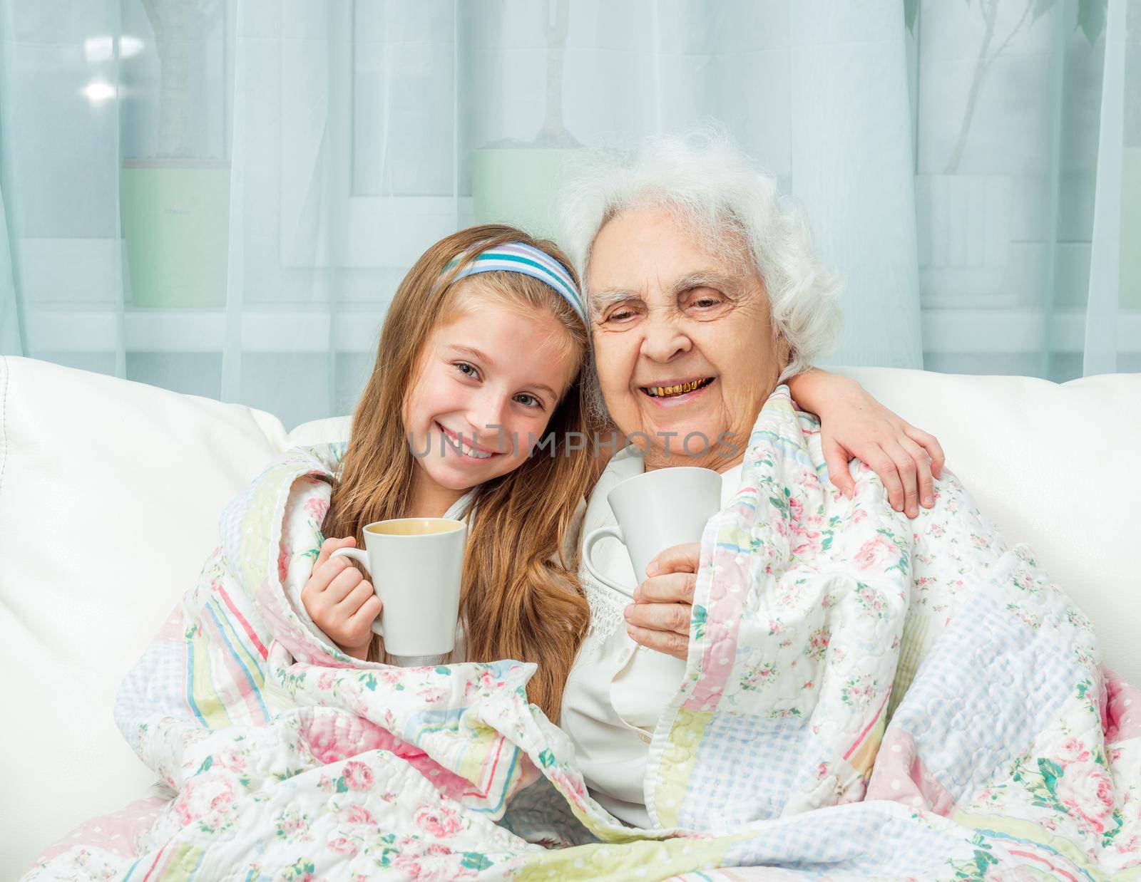 grandmother and granddaughter drink tea covered with blanket